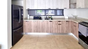A modern kitchen with wooden cabinets, a stainless steel refrigerator, and a gas stove. - Casa de las Olas (La Paz)