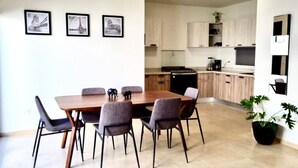 A modern dining area with a wooden table and grey chairs, a kitchen with light wood cabinets, and three framed pictures on the wall. - Casa de las Olas (La Paz)