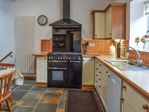 A compact kitchen with a stove, oven, sink, and wooden cabinets. - 3 bedroom accommodation in Lydney (Lydney)