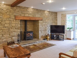 A stone-walled room with a fireplace, a television on a stand, and a wooden table.