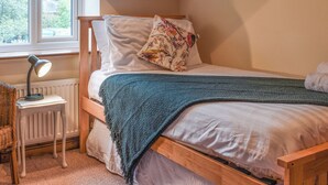Un dormitorio acogedor con una cama de madera, una mesita de noche pequeña con una lámpara y una ventana con vista a follaje.