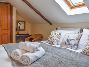 A bedroom with a skylight, a bed with rolled towels, a wicker chair, and patterned pillows.