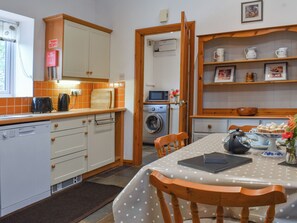 A compact kitchen with a dining area, featuring a washing machine, a microwave, and a sink. - 3 bedroom accommodation in Lydney (Lydney)