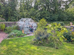 A greenhouse in a garden with various plants and a stone wall in the background. - 3 bedroom accommodation in Lydney (Lydney)