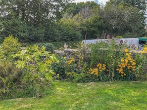 A garden with various plants and flowers, a stone wall, and a green structure in the background. - 3 bedroom accommodation in Lydney (Lydney)