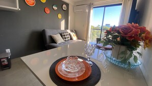 Una sala moderna con una mesa de comedor preparada para dos personas, un sofá con cojines estampados, un jarrón con flores y platos decorativos colgados en la pared.