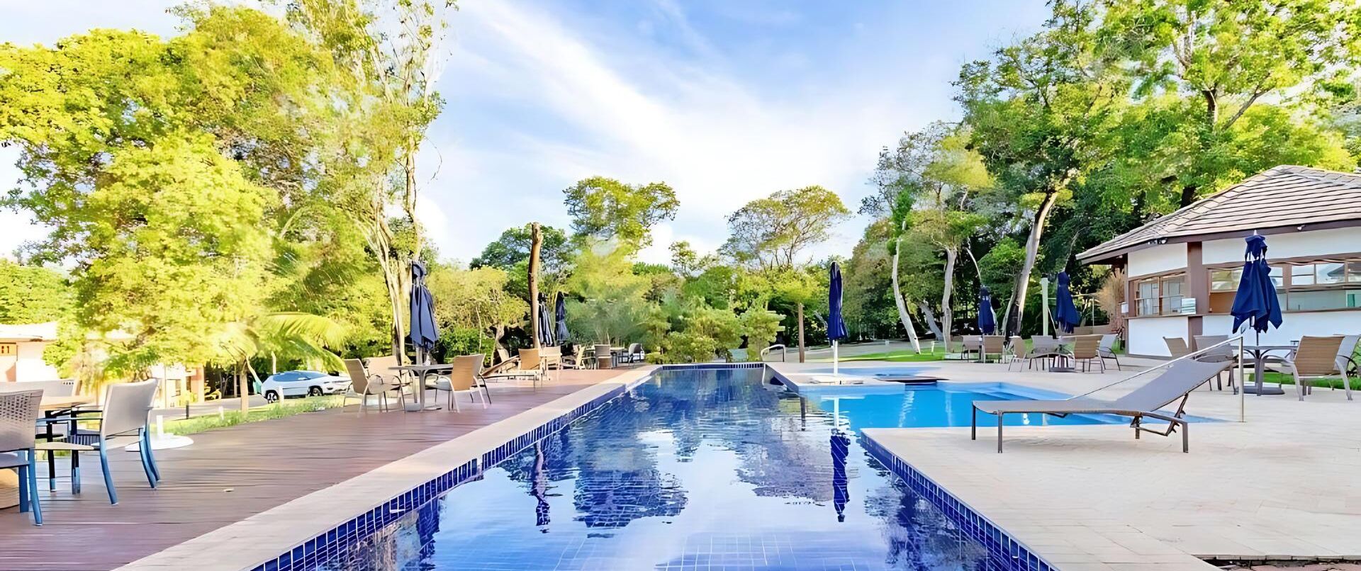 A swimming pool with lounge chairs and umbrellas, surrounded by trees and a building.