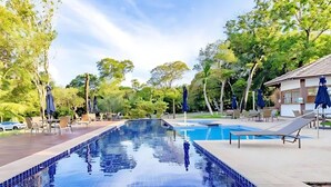 A swimming pool with lounge chairs and umbrellas, surrounded by trees and a building. - Apartment 2/4 Reserva Timeantube Praia do Forte - Comfort and Leisure in Nature (Açu da Torre)