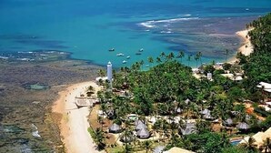 A coastal resort with a beach, palm trees, and a lighthouse. - Apartment 2/4 Reserva Timeantube Praia do Forte - Comfort and Leisure in Nature (Açu da Torre)