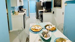 Un comedor con una mesa preparada para cuatro, una cocina al fondo y una pared azul.