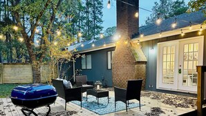 Un patio trasero con una parrilla, mobiliario exterior e iluminación colgante.