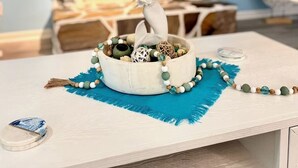 Una habitación con pared de piedra, una mesa blanca con un objeto decorativo y un tapete azul.