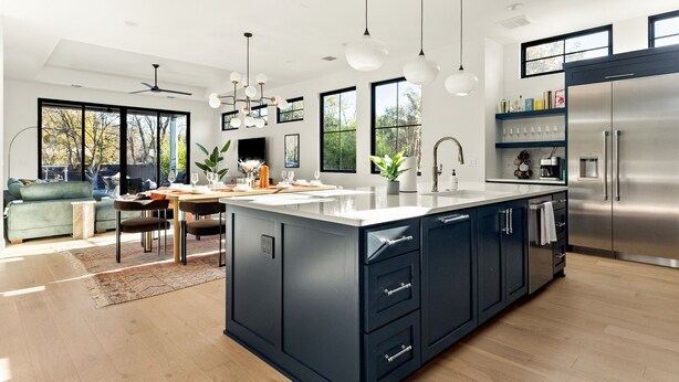 Una cocina moderna con una isla grande, muebles oscuros, electrodomésticos de acero inoxidable e iluminación colgante.