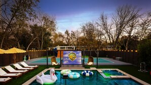 Un patio trasero con piscina, un cisne inflable, sillas de descanso y un logotipo de Warner Bros.