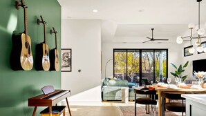 Una sala de estar moderna con un piano, una zona de comedor con una mesa dispuesta para dos personas y un ventanal con vistas a árboles.