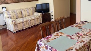 A living room with a sofa, a dining table with chairs, a television, and a large painting on the wall. - Suite51 - Cozy apartment in Porta Romana near the center (Milano)
