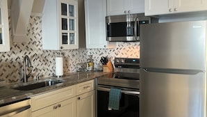 Una cocina moderna con armarios blancos, electrodomésticos de acero inoxidable, un salpicadero con diseño y suelo de madera.