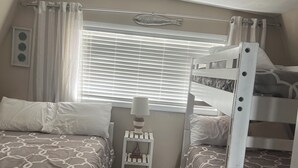 Un dormitorio con literas, una mesita de noche con lámpara, una ventana con persianas y una decoración de peces en la pared.