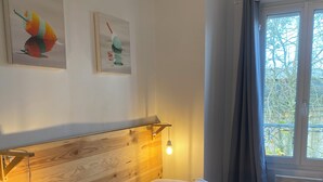 En pænt redt seng med hvide sengetøj og puder, et træsengegærde med hængende lamper, samt to billeder hængt på væggen.