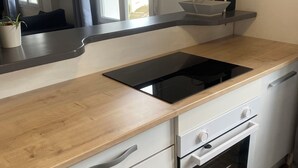 Et moderne køkken med træbordplade, hvide skabe, en indbygget ovn og et vindue med gardiner.