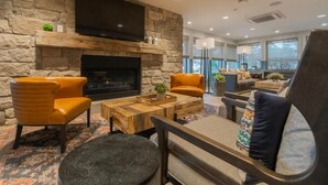 A modern living room with a stone fireplace, leather armchairs, and a flat-screen TV.