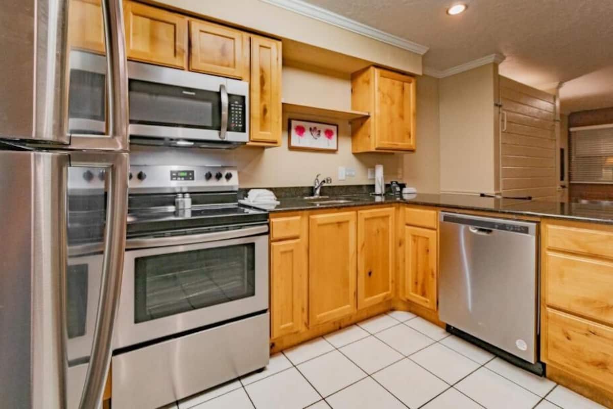 A modern kitchen with stainless steel appliances, wooden cabinets, and a tiled floor.