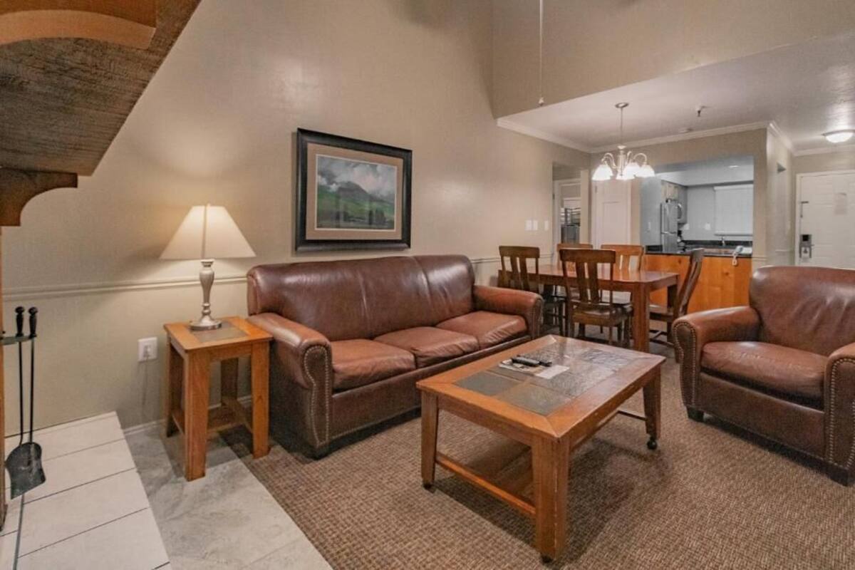 A living room with a brown leather sofa, wooden coffee table, and a dining area with wooden chairs and a table.