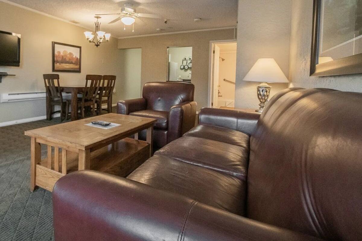 A living room with a leather sofa, wooden coffee table, and a TV mounted on the wall.