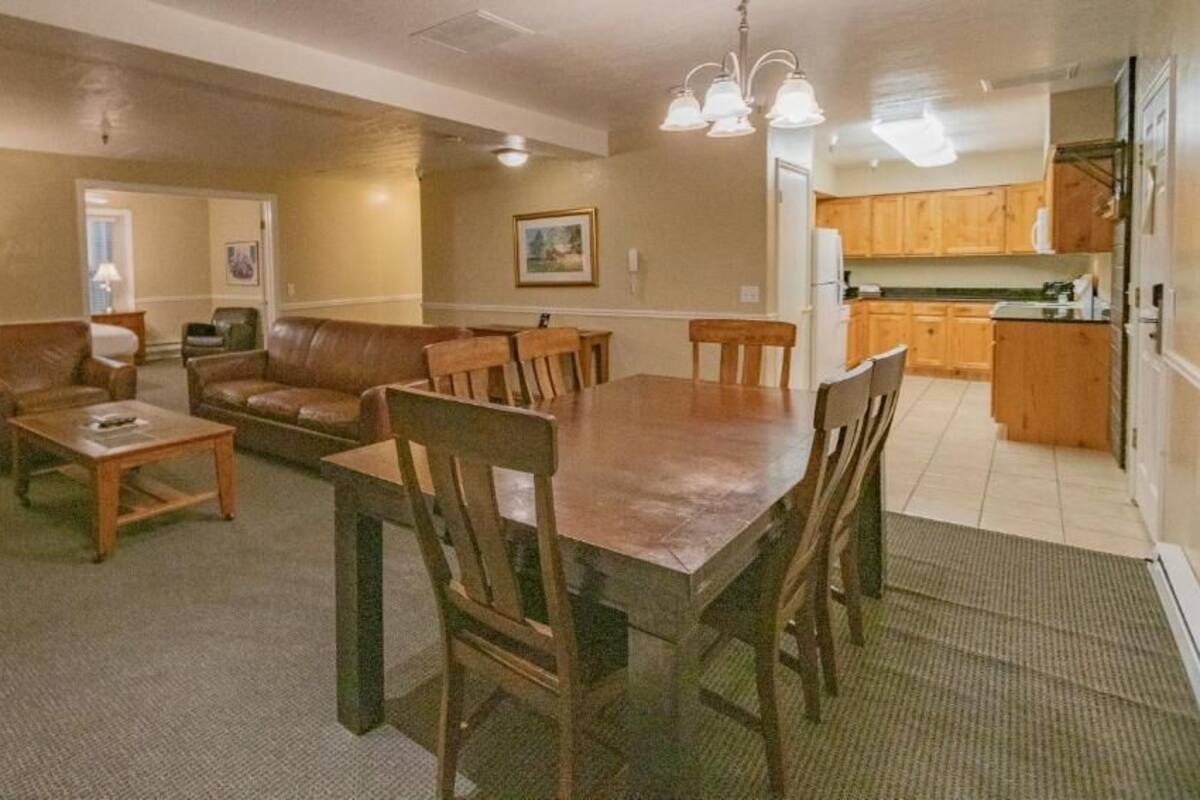 A spacious living room with a dining table and chairs, a leather sofa, and a kitchen area with wooden cabinets.