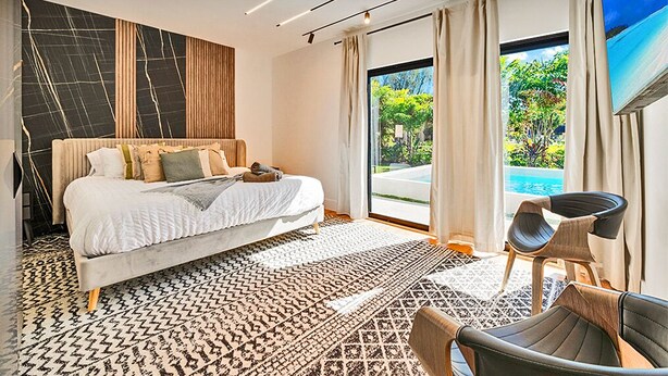 Una habitación de hotel moderna con una cama grande, vistas a una piscina y un balcón.