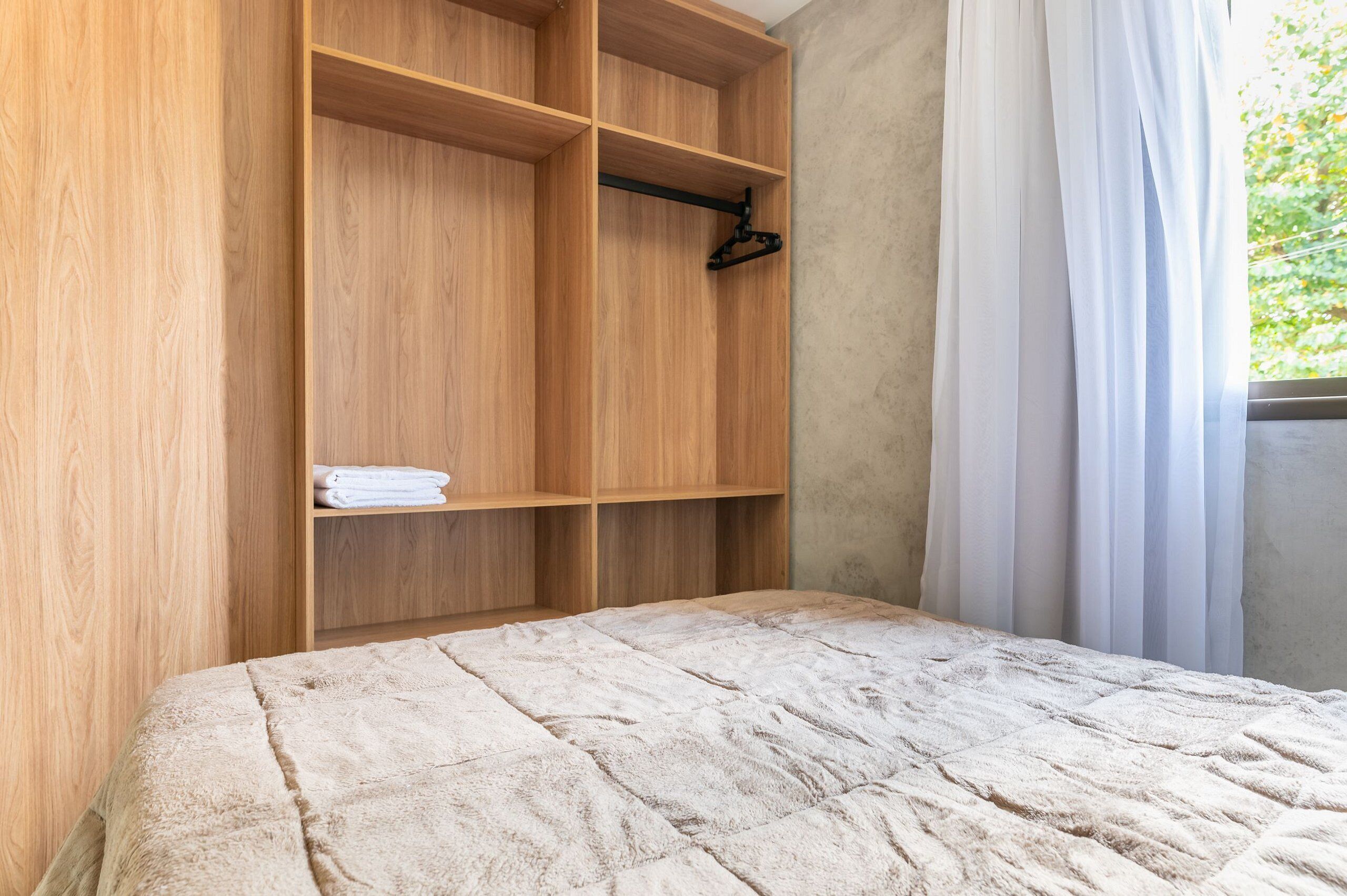 A bedroom with a bed, wooden wardrobe, and a window with curtains.