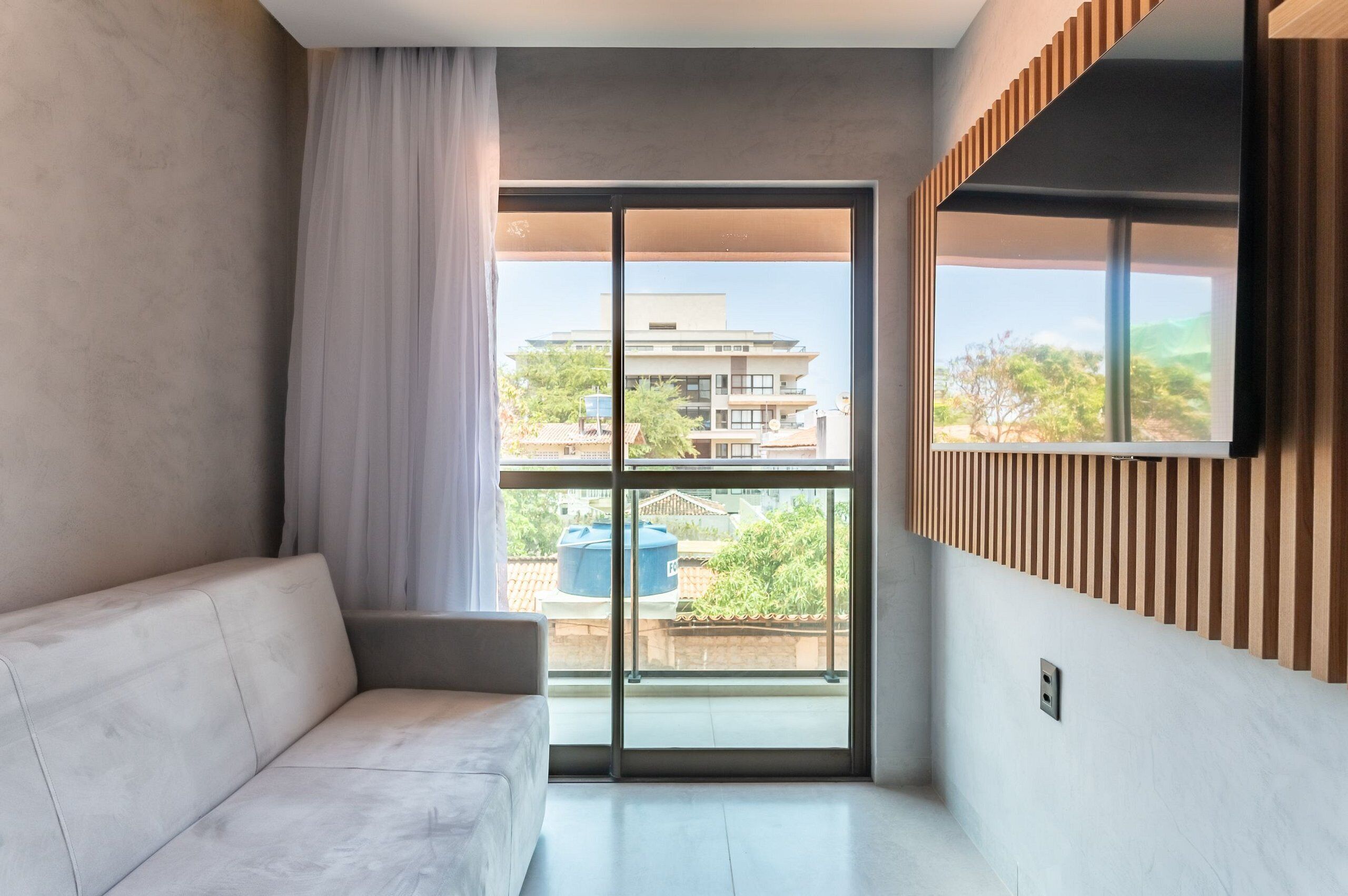 Una sala moderna con un sofá, un amplio ventanal corredero y vistas a edificios y zonas verdes.