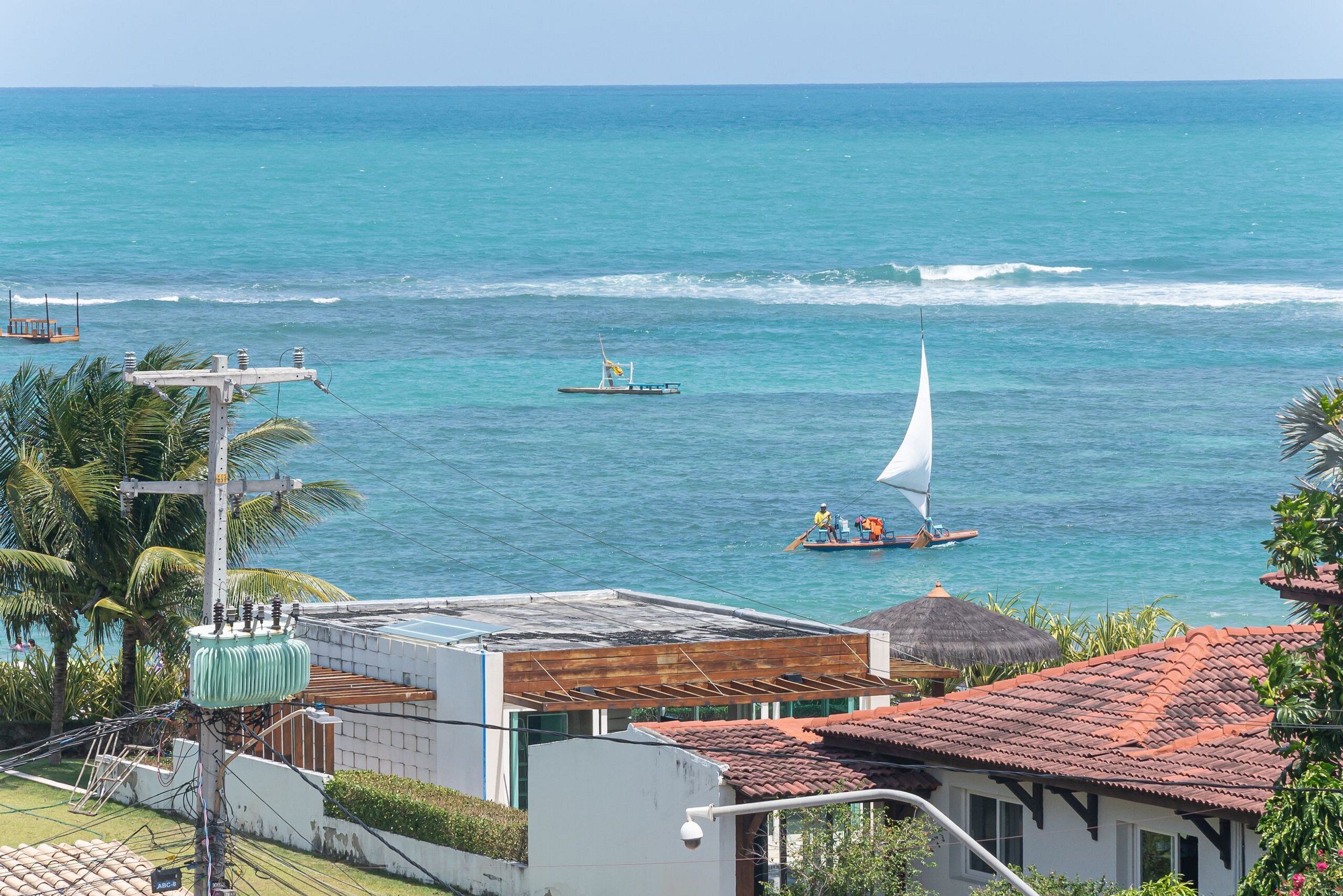 Une vue sur la côte, avec un voilier, un petit bateau à moteur et un bâtiment surmonté d’un toit recouvert de tuiles rouges.