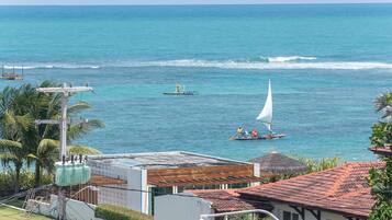 Une vue sur la côte, avec un voilier, un petit bateau à moteur et un bâtiment surmonté d’un toit recouvert de tuiles rouges.