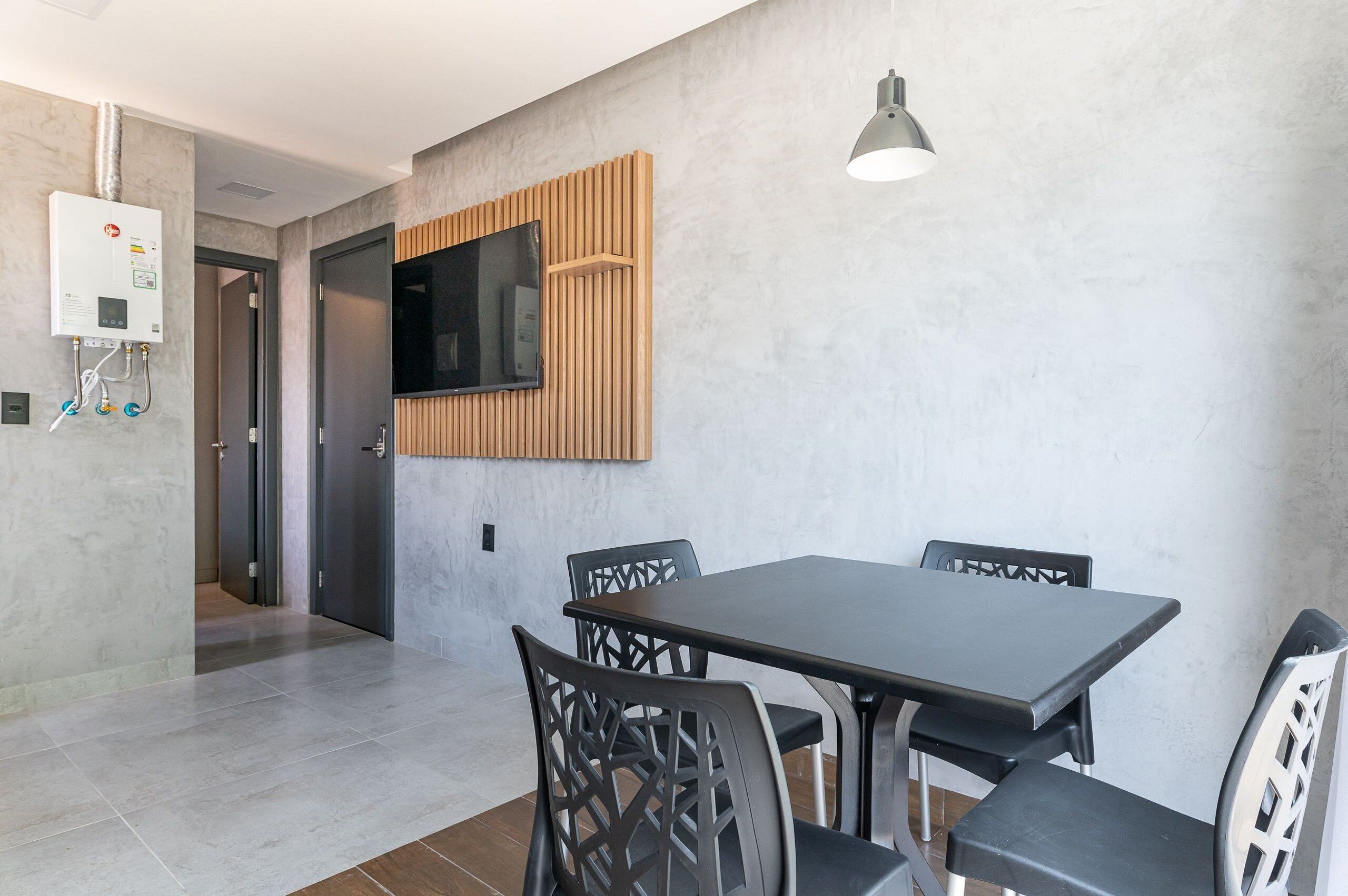 Un comedor moderno con una mesa rectangular y cuatro sillas, un televisor de pantalla plana montado en la pared y una lámpara colgante.