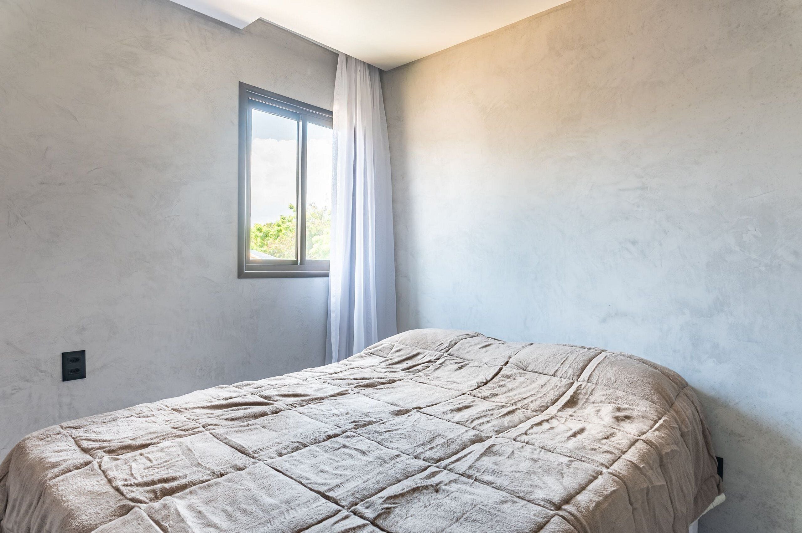 Une chambre à coucher avec un lit, une fenêtre avec des rideaux et un mur uni.