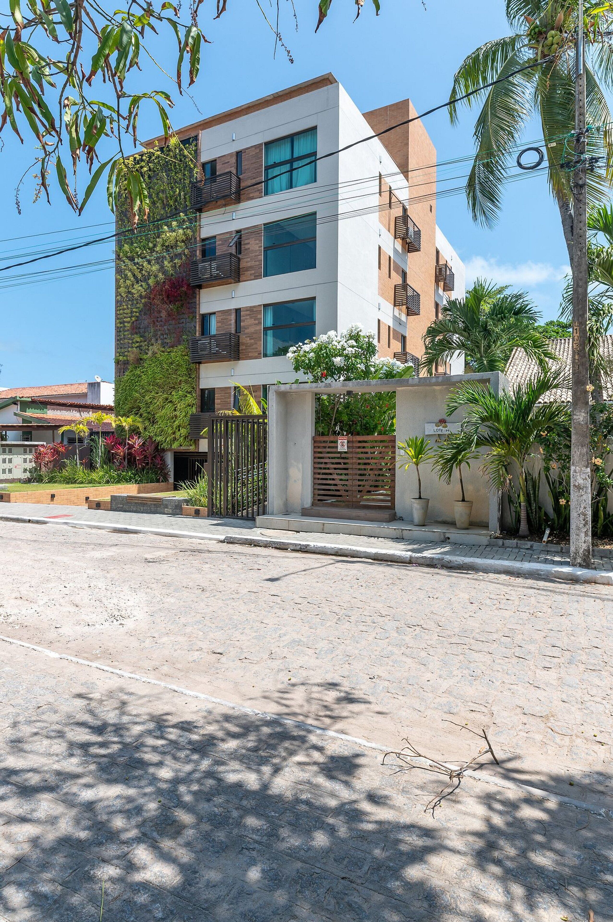 A modern multi-story building with balconies, a gated entrance, and potted plants.