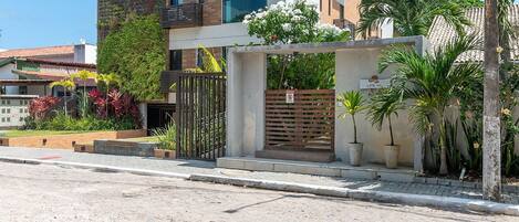 A modern multi-story building with balconies, a gated entrance, and potted plants.