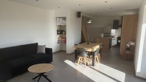 Ein modernes Wohnzimmer mit einer Couch, einem runden Couchtisch und einem Essbereich mit Holztisch und Stühlen. Im Hintergrund ist eine Küche zu sehen.