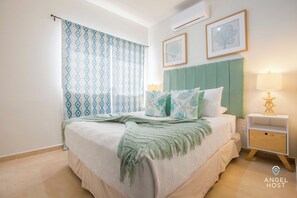 Un dormitorio con cama, mesita de noche, lámpara y dos cuadros en la pared.