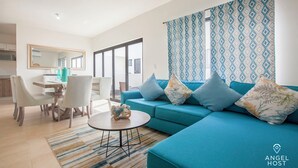 A modern living room with a teal sofa, a dining area with white chairs, and a kitchen in the background. - Family Homes with Pool and Playground (La Paz)