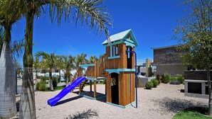 A playground with a slide and climbing structures, surrounded by palm trees and a building labeled "Hispaniola". - Family Homes with Pool and Playground (La Paz)