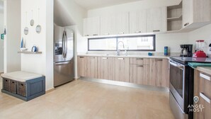 A modern kitchen with light wood cabinets, stainless steel appliances, and a large window providing natural light. - Family Homes with Pool and Playground (La Paz)