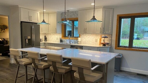 Una cocina moderna con una isla grande, taburetes de bar, lámparas colgantes y vistas al exterior.