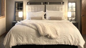 Una cama grande con colcha blanca, dos mesitas de noche con lámparas y una puerta de madera.