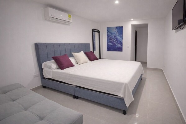 A modern bedroom with a grey upholstered bed, white linens, and purple pillows.