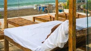 Un cabanon de plage doté de mobilier en bois et surmonté d’un auvent blanc, offrant une vue sur l’océan.