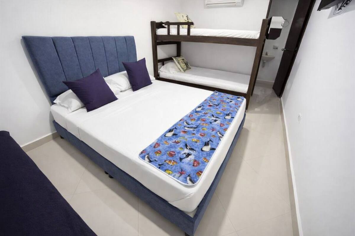 A single bed with a blue headboard and white bedding, a bunk bed to the right, and a blue patterned blanket.