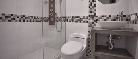 Une salle de bain moderne avec une douche à parois de verre, des toilettes blanches et un lavabo avec un dosseret de carrelage à motifs.