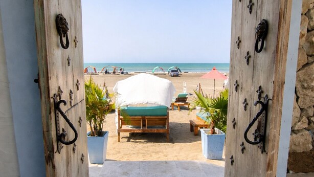 Une porte en bois donnant sur une plage, avec un lit et des chaises longues.